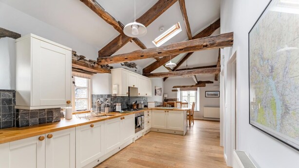 A kitchen with wooden beams, white cabinets, a wooden countertop, and a large map on the wall. - 1 Bed in Ambleside (oc-lr160) (Ambleside)