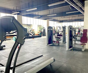 Ein Fitnessraum mit Trainingsgeräten, Laufband und großen Fenstern für natürliches Licht.
