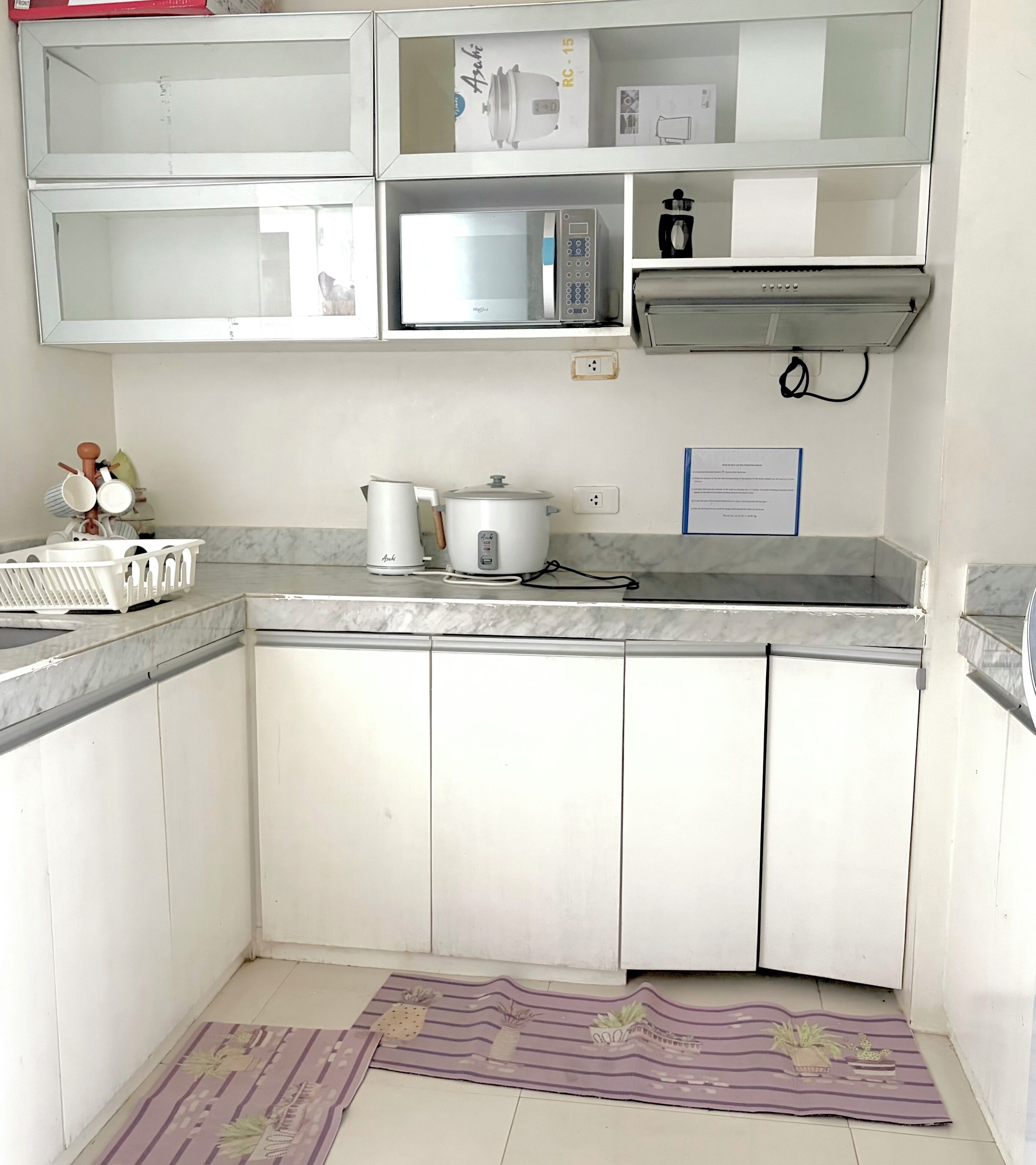 Una cocina compacta con armarios blancos, microondas, cafetera y refrigerador pequeño.