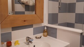 A bathroom with a white sink, a mirror, a towel rack, a shower, and a bottle of soap. - Belle Dune Apartment: Between the Lake, the Sea, and the Pine Forest (Fort Mahon)