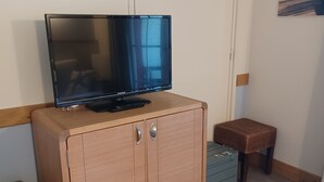 A television on a wooden cabinet, a small stool, and a blue storage box. - Belle Dune Apartment: Between the Lake, the Sea, and the Pine Forest (Fort Mahon)