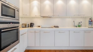 A modern kitchen with white cabinets, a built-in oven, a coffee maker, and a sink with cleaning supplies. - 2 Bed in Ambleside (oc-lr211) (Claife)