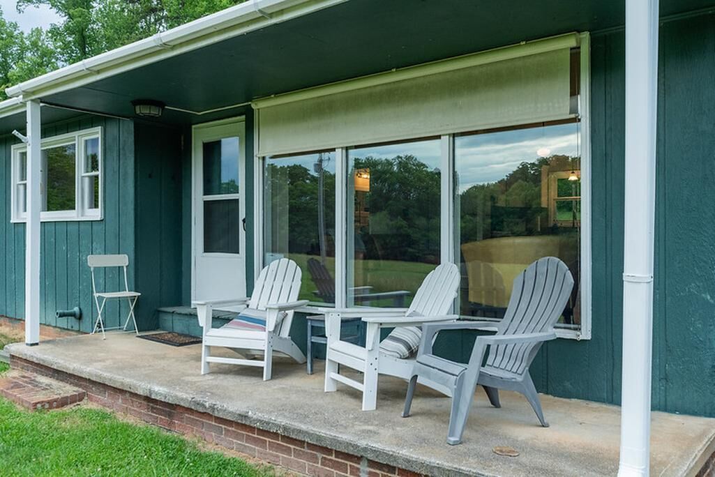 Eine Veranda mit drei Adirondack-Stühlen, einem kleinen Tisch und einem Fenster mit Blick ins Freie.