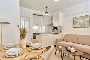 A modern kitchen with white cabinets, a central island, and a dining area with a table set for four. - Suite for 4- Arc de Triomphe Faubourg Saint-Honoré (Paris)