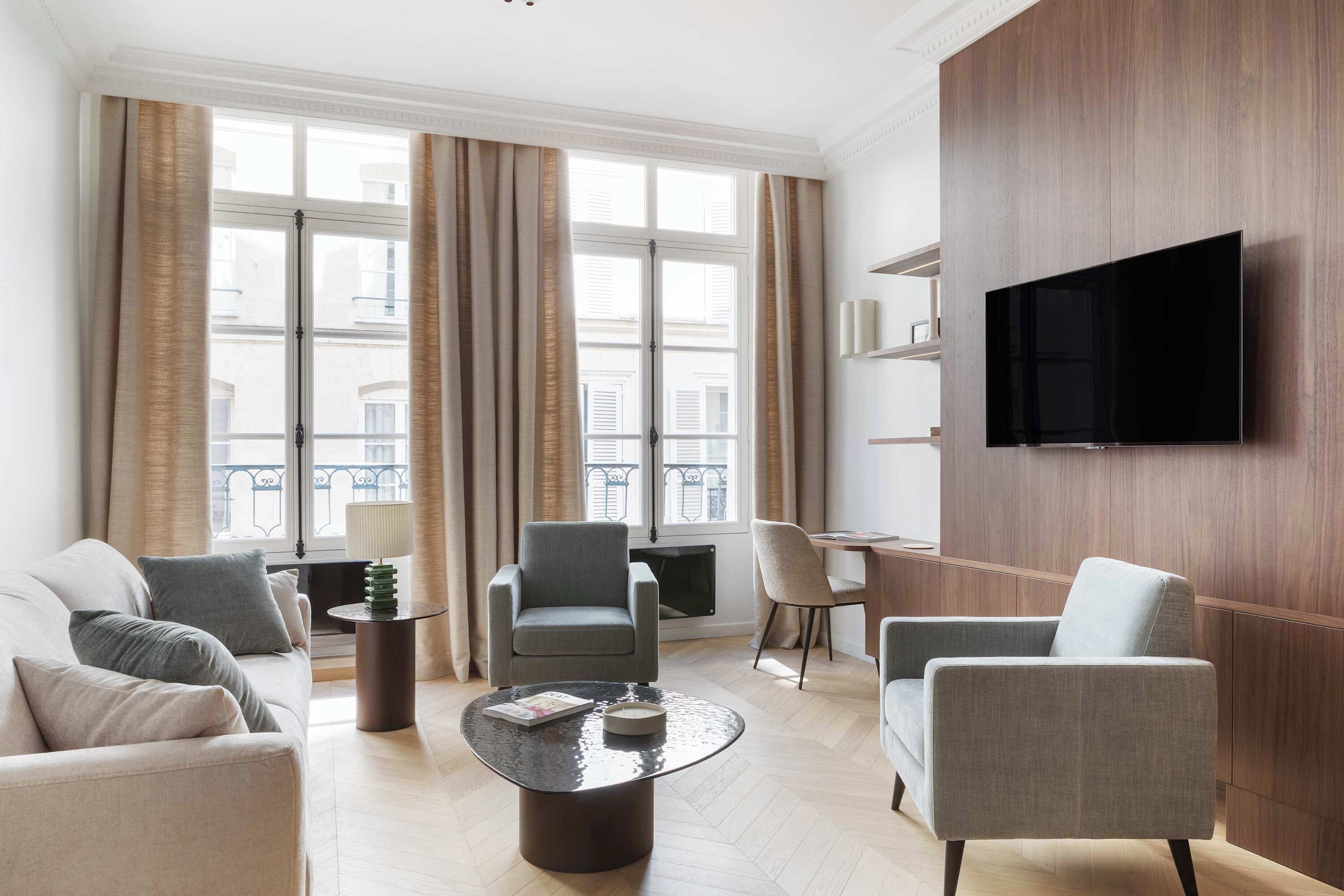 Ett modernt vardagsrum med en soffa, fåtöljer, ett soffbord, en tv och ett stort fönster med gardiner.