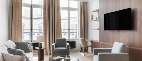 Un salon moderne comprenant un canapé, des fauteuils, une table basse, un téléviseur et une grande fenêtre avec des rideaux.