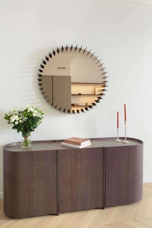 A modern, dark-toned console table with a round mirror, a vase of flowers, and two red candles. - Luxurious Apartment 1Bdr Saint Germain des Prés (Paris)
