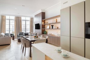 A modern living room with a dining area, a kitchen with built-in appliances, and a large window with curtains. - Luxurious Apartment 1Bdr Saint Germain des Prés (Paris)