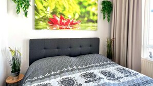 Une chambre avec un lit, un grand tableau accroché au mur et deux plantes suspendues.