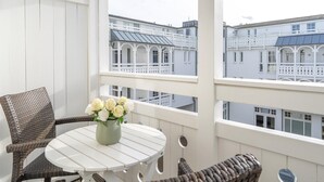 Un balcon agrémenté de meubles en osier, d’une table blanche et d’un vase de fleurs.