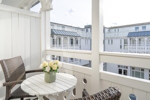 Ein Balkon mit Korbmöbeln, einem weißen Tisch und einem Blumenstrauß.