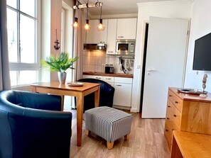 A compact kitchen with a dining area, a potted plant, and a television on a stand. - Kompakte Ferienwohnung im Seepark Sellin mit Balkon (Sellin)