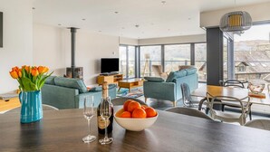 Una sala de estar moderna con un sofá, una mesa de comedor con fruta y copas de vino, y un televisor.