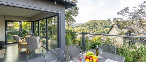 Ein moderner Essbereich im Freien mit Glaswand, Tisch gedeckt mit Obstschale, Weingläsern und einer Speisekarte.