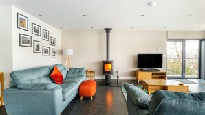 Una sala de estar moderna con un sofá, reposapiés, chimenea, televisor y una obra de arte en la pared.