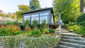 Una casa moderna con un muro de piedra, una escalera de madera y un jardín con diversas plantas y flores.