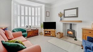 Una sala de estar con sofá, televisión, chimenea y ventana con contraventanas.