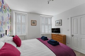 A bedroom with a bed, two windows with shutters, a dresser, a television, and a door. - 3 Bed in Windermere (oc-lr195) (Windermere)