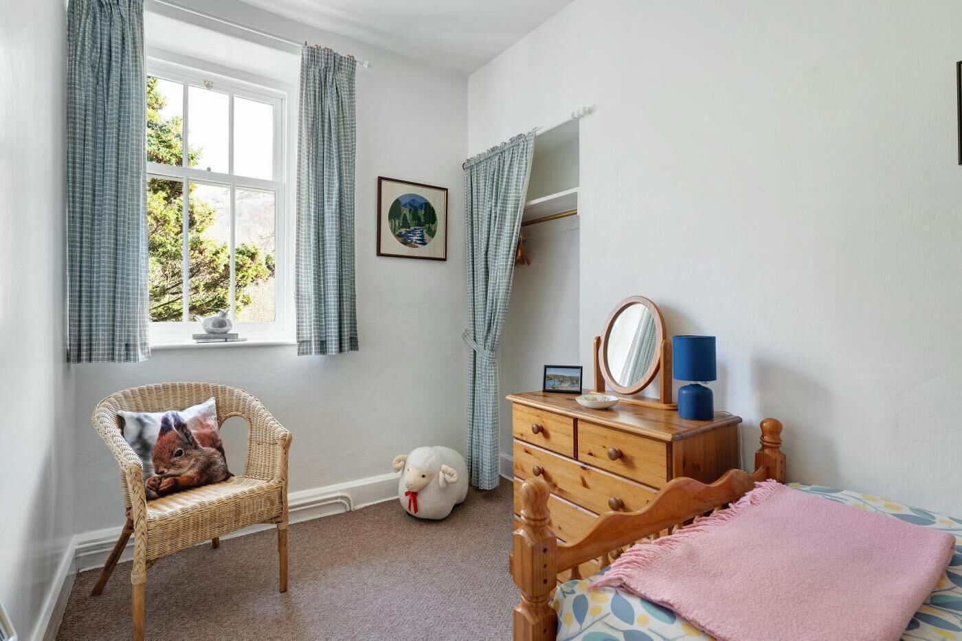 A bedroom with a bed, a dresser, a chair, a window with curtains, a wall-mounted mirror, and a framed picture.