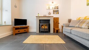 A living room with a fireplace, a television on a wooden stand, a sofa, and a rug. - 1 Bed in Ambleside (oc-lr036) (Ambleside)