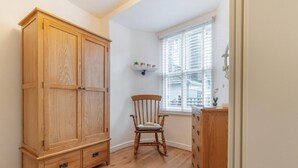 A room with a wooden wardrobe, a wooden chair, a window with blinds, and a small shelf with decorative items. - 1 Bed in Ambleside (oc-lr036) (Ambleside)