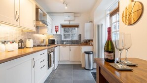 A modern kitchen with white cabinets, a stainless steel range hood, a coffee maker, and a wine bottle on the counter. - 1 Bed in Ambleside (oc-lr036) (Ambleside)