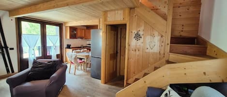 A wooden interior with a sofa, a dog, a staircase, and a kitchen area.