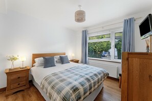 A bedroom with a bed, bedside tables, a lamp, a window with curtains, and a TV on a wooden cabinet. - 2 Bed in Ambleside (oc-lr191) (Ambleside)