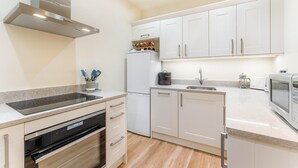 Een moderne keuken met witte kastjes, een roestvrijstalen afzuigkap, een inbouwoven, een vaatwasser, een spoelbak en een magnetron.