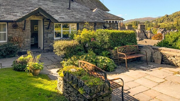 Een stenen huis met een schuin dak, een tuin met een bankje en een helder uitzicht over de omliggende heuvels.
