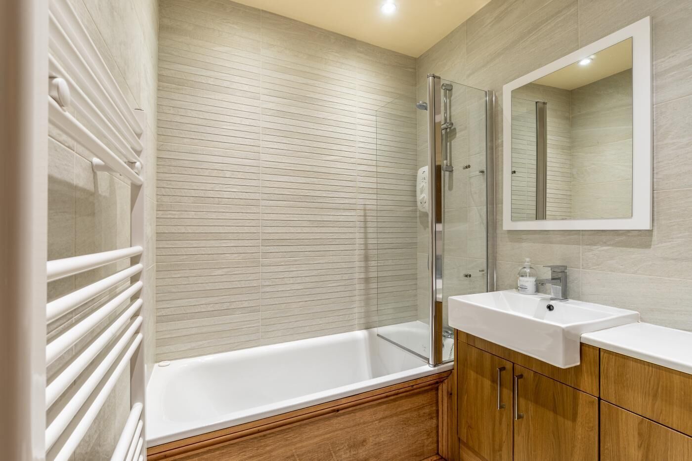 A modern bathroom with a glass-enclosed shower, a white bathtub, wooden cabinets, and a large mirror.