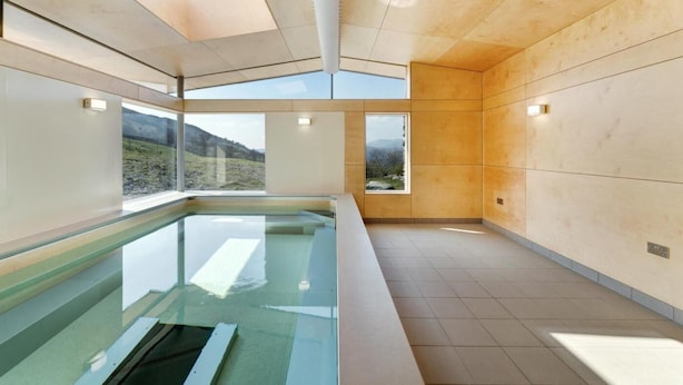 A modern indoor swimming pool with large windows, wooden walls, and a tiled floor. - 1 Bed in Ambleside (oc-lr175) (Ambleside)