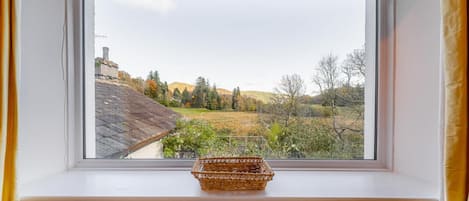 A window with a view of a rural landscape, a wicker basket on the sill, and a white wall.