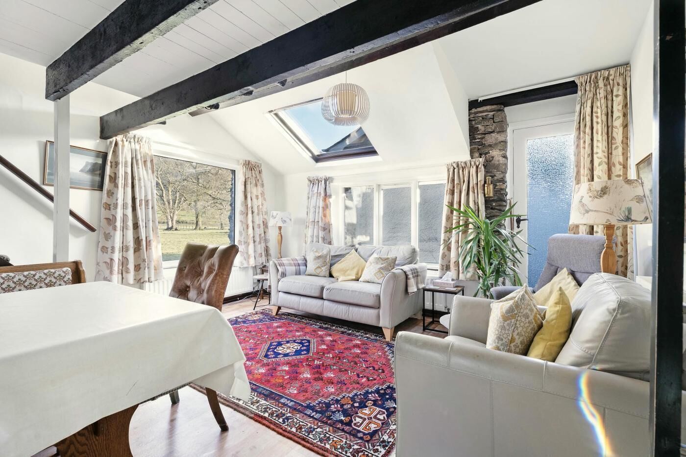 A spacious living room with a high ceiling, a skylight, a large rug, and a dining area with a table.