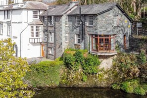 A stone building with a balcony overlooking a body of water, surrounded by greenery. - 1 Bed in Ambleside (oc-lr119) (Ambleside)