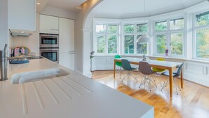 A modern kitchen with white cabinetry, a central island, and a dining area with a table and colorful chairs. - 2 Bed in Ambleside (oc-lr218) (Claife)