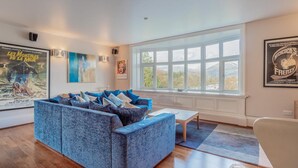 A living room with a blue sofa, a white armchair, a coffee table, and a large window with a view. - 2 Bed in Ambleside (oc-lr218) (Claife)