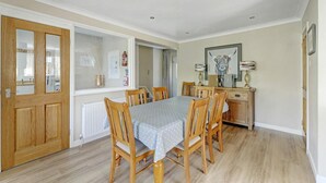 A dining area with a table set for six, wooden chairs, a radiator, a wooden cabinet, and a framed artwork on the wall. - 4 Bed in Ambleside (oc-lr120) (Ambleside)