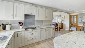 A kitchen with white cabinets, a granite countertop, and a dining area with a table and chairs. - 4 Bed in Ambleside (oc-lr120) (Ambleside)