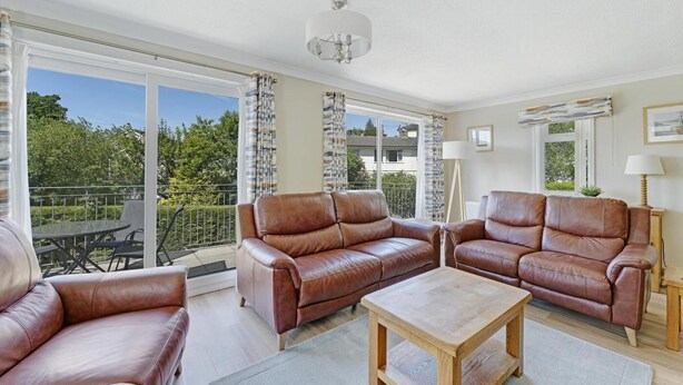A spacious living room with leather sofas, a wooden coffee table, and large windows offering a view of the outdoors. - 4 Bed in Ambleside (oc-lr120) (Ambleside)