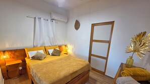 A bedroom with a wooden bed, bedside lamps, a wall-mounted air conditioner, a wooden wardrobe, and a small table with a vase. - Tiny Ôm, water tank, and pools (Saint-François)