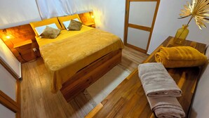 A bed with a wooden headboard, a bedside table with a lamp, and a bench with towels. - Tiny Ôm, water tank, and pools (Saint-François)