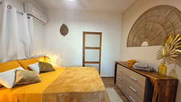 A bedroom with a bed, bedside table, dresser, and a wall-mounted fan. - Tiny Ôm, water tank, and pools (Saint-François)