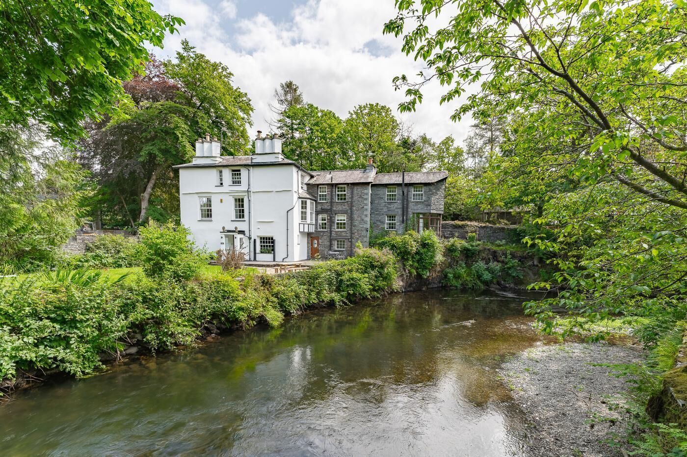 Een pand aan de rivier met een wit gebouw en een stenen constructie, omgeven door weelderige begroeiing.