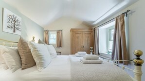 Une chambre à coucher avec un grand lit, une armoire en bois, une fenêtre avec des rideaux et un tableau accroché au mur.