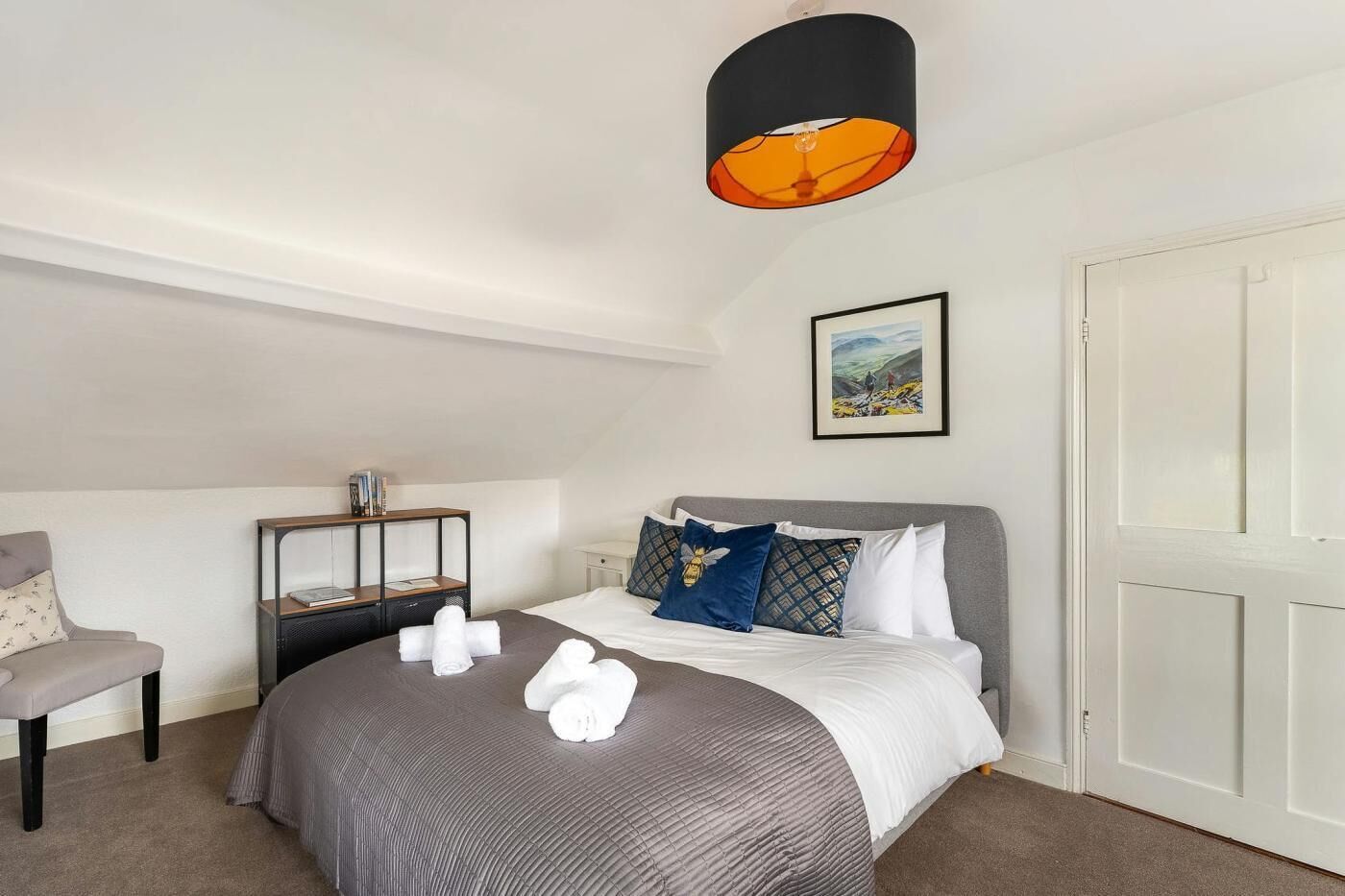 Een slaapkamer met een bed, nachtkastje, stoel, hanglamp en een ingelijst schilderij aan de muur.