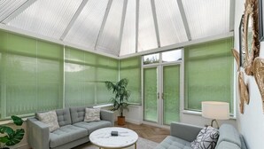 Ein Wintergarten mit einem grauen Sofa, einem runden Couchtisch und einer Topfpflanze.