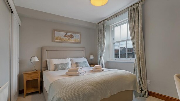 A bedroom with a bed, bedside tables, a lamp, a window with curtains, and a painting on the wall. - 3 Bed in Windermere (oc-lr044) (Windermere)