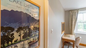 A room with a framed poster of Lake District National Park, a wooden desk, a chair, and a window with curtains. - 3 Bed in Windermere (oc-lr044) (Windermere)