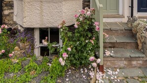 A corner bay window with a stone facade, a green door with the number 33, and a flower bed with pink roses. - 3 Bed in Windermere (oc-lr044) (Windermere)
